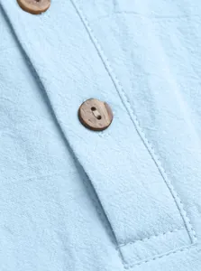 Detailed close-up of light blue linen polo shirt fabric with two brown wood buttons