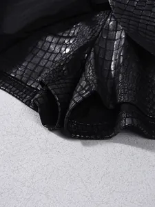 Detail of black faux leather skirt with embossed crocodile texture and glossy coating