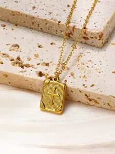 Detail of a gold rectangular pendant with cross relief on a beige stone background