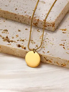 Detailed close-up of a polished gold round pendant with a sleek snake chain on stone