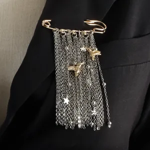 Dettaglio di spilla con nappine metalliche e ciondoli ape e stella su blazer nero