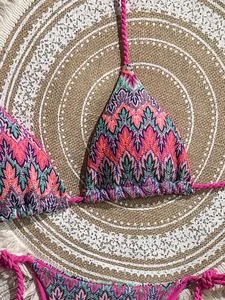 Flat lay of colorful geometric pattern bikini set on a woven bohemian beach mat