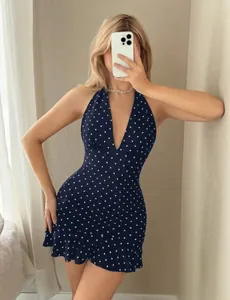 Detail of navy blue polka dot halter dress featuring a deep V-neck and ruffled hemline