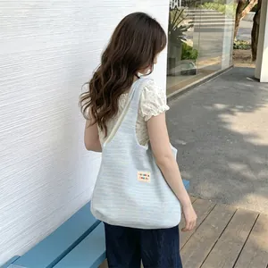 Outdoor shot of a light blue knit tote bag showing thick texture and woven logo tag