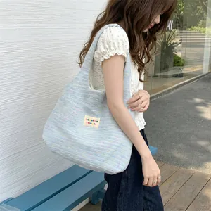 Detail of light blue knit tote bag with rainbow texture and brand woven label