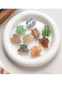 Flat lay of small acetate hair claws in various colors arranged on a white ceramic tray