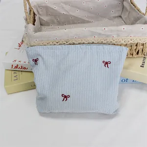 Detail of red bow embroidery on blue and white striped fabric toiletry storage bag
