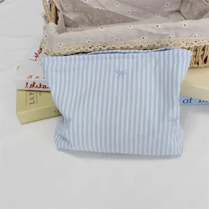 Detail of blue striped makeup bag featuring delicate bow embroidery and soft cotton texture