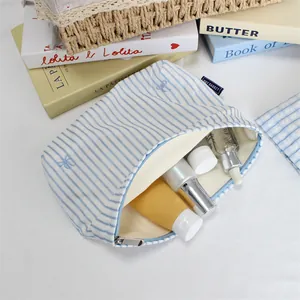 Detail of blue striped canvas makeup bag with bow embroidery and metal zipper closure