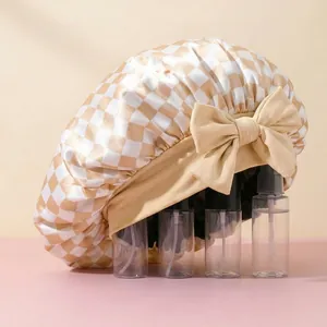Close-up of satin hair bonnet featuring beige checkered pattern and large decorative bow