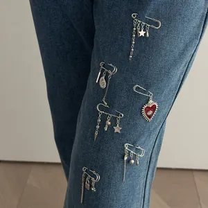 Close-up of silver brooch pins with heart and star pendants on denim fabric