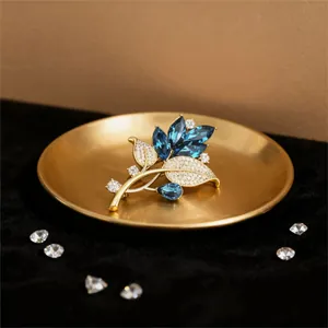 Detailansicht der goldenen Blattbrosche mit blauen Edelsteinen und weißen Kristallen