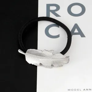 Macro view of metallic silver leaf charm detail on elastic black hair scrunchie