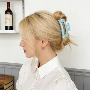 Blue checkered PVC hair claw clip displayed on blonde hair in a cozy interior