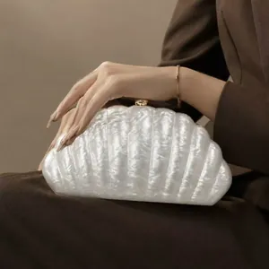 Detailed close-up of white shell-shaped evening clutch bag with golden metal clasp