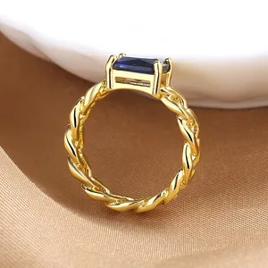 Detail of a gold twisted band ring with a rectangular blue gemstone in four-prong setting