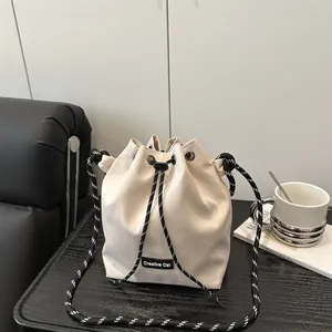 Dettaglio borsa a secchiello bianco panna con tracolla intrecciata e logo Creative Cat
