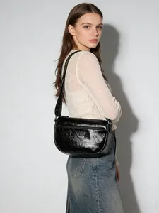 Détail du sac bandoulière en cuir noir brillant avec texture plissée et large sangle