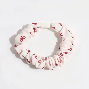 Beige scrunchie with red bow pattern and elastic core for gentle hair styling