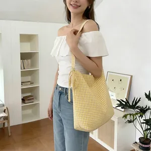 Detail of yellow checkered canvas tote bag with adjustable bow shoulder strap on a model