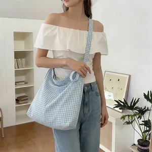 Close-up of blue gingham canvas hobo bag with wide shoulder strap on a model