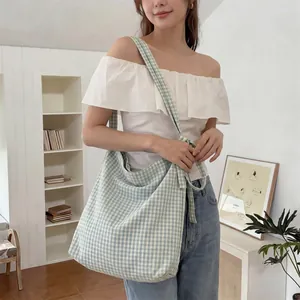 Close-up of large green gingham canvas tote bag worn by model in cozy home setting