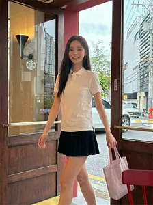 Outdoor shot of a woman in a white polo shirt, black pleated skirt, and pink tote bag