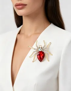 Close-up of a rhinestone spider brooch with a red pear-shaped crystal on a white top