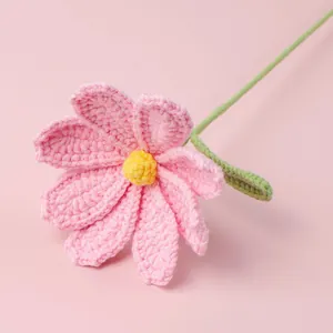Pink handmade crochet daisy with yellow pistil and green leaf on pink background