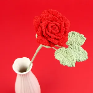 Handmade crochet red rose with green leaves in a white ceramic vase on red background