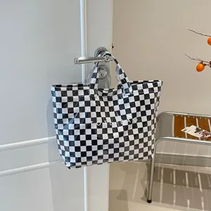 Checkered tote bag with letter print hanging on a white door in a minimalist setting