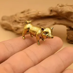 Detailed macro shot of a miniature brass pig figurine resting on a fingertip