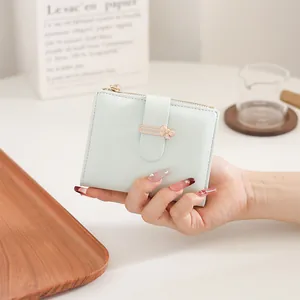 Close-up of mint green short leather wallet with gold bow clasp and zipper closure