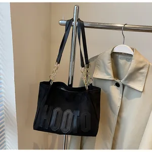 Detail of black suede tote bag featuring HOOTO lettering and gold chain straps