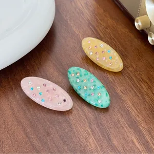 Three-piece oval acetate hair clips with colorful rhinestones on a vintage background