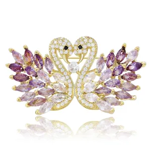 Elegant gold-tone double swan brooch featuring purple gemstones and micro-set crystals
