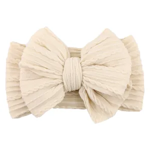 Creamy white knitted baby headband with a large jacquard bow and cable knit pattern