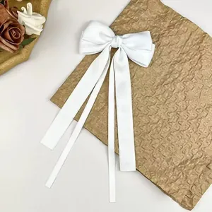 Elegant white satin hair clip with long ribbon bow in a graceful floral setting