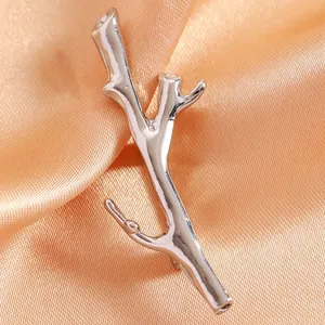 Close-up of polished silver branch brooch resting on soft peach satin fabric