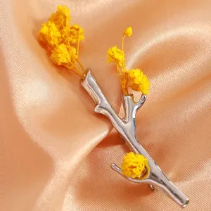 Detail of silver branch-shaped brooch with yellow dried flowers on satin background