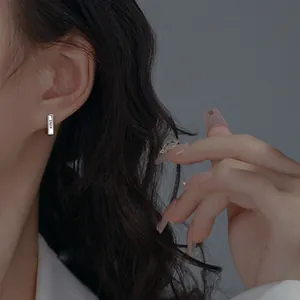 Close-up of silver geometric bar earrings with LUCKY engraving on a person's ear