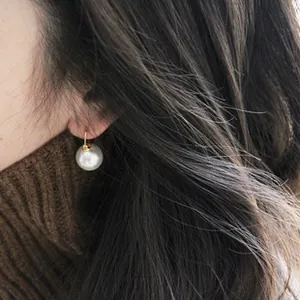 Close-up of elegant white round faux pearl earrings with gold clasp on model's ear