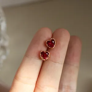 Detailed close-up of red heart-shaped zircon earrings with gold plating on a finger