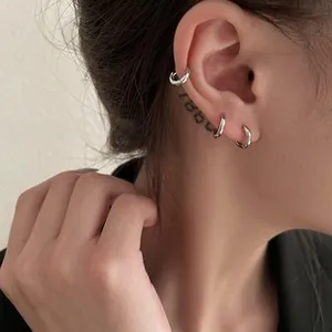Close-up of minimalist silver hoop earring and cuff on ear with polished finish