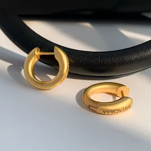 Close-up of gold huggie hoop earrings featuring engraved brand lettering on the side