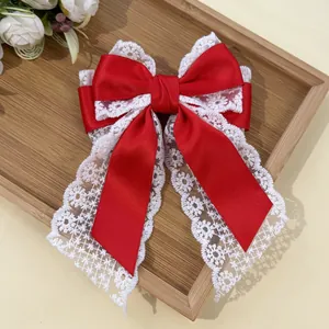 Detail of red satin bow hair clip with white floral lace trim and long ribbons
