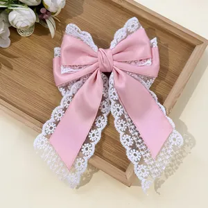 Close-up of pink silk bow hair clip with white floral lace trim on a wooden tray