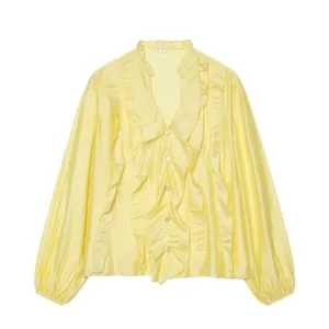 Close-up of V-neck ruffle detailing and white buttons on a pale yellow satin shirt