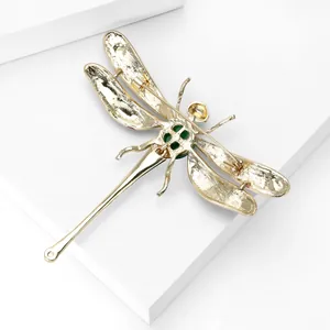 Broche libellule créative dorée avec émail vert sur fond blanc minimaliste