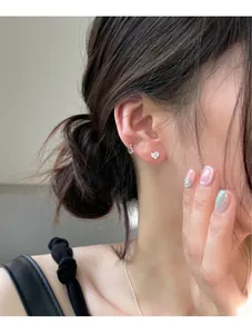 Close-up of heart stud and silver ear cuff with zircons worn on a model ear